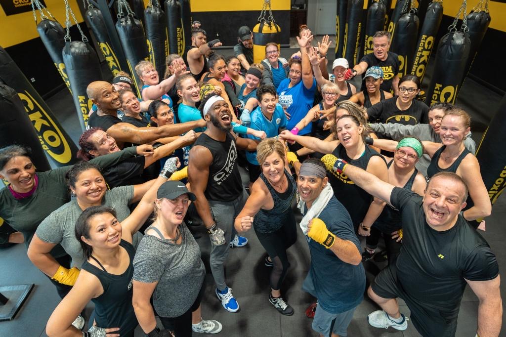 A packed cardio boxing class cheering together under the heavy bags